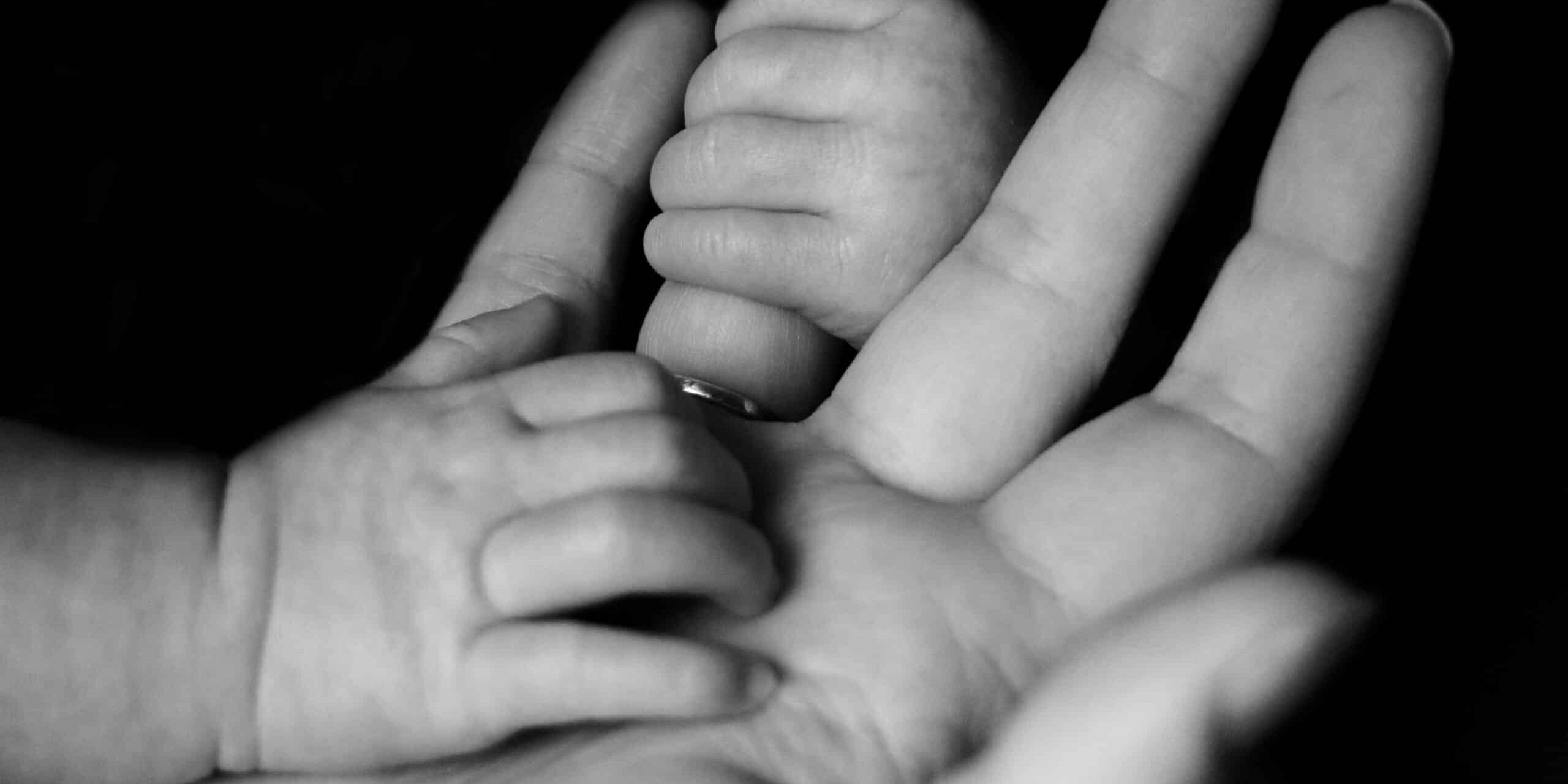 Two baby hands hold onto the hand of an adult