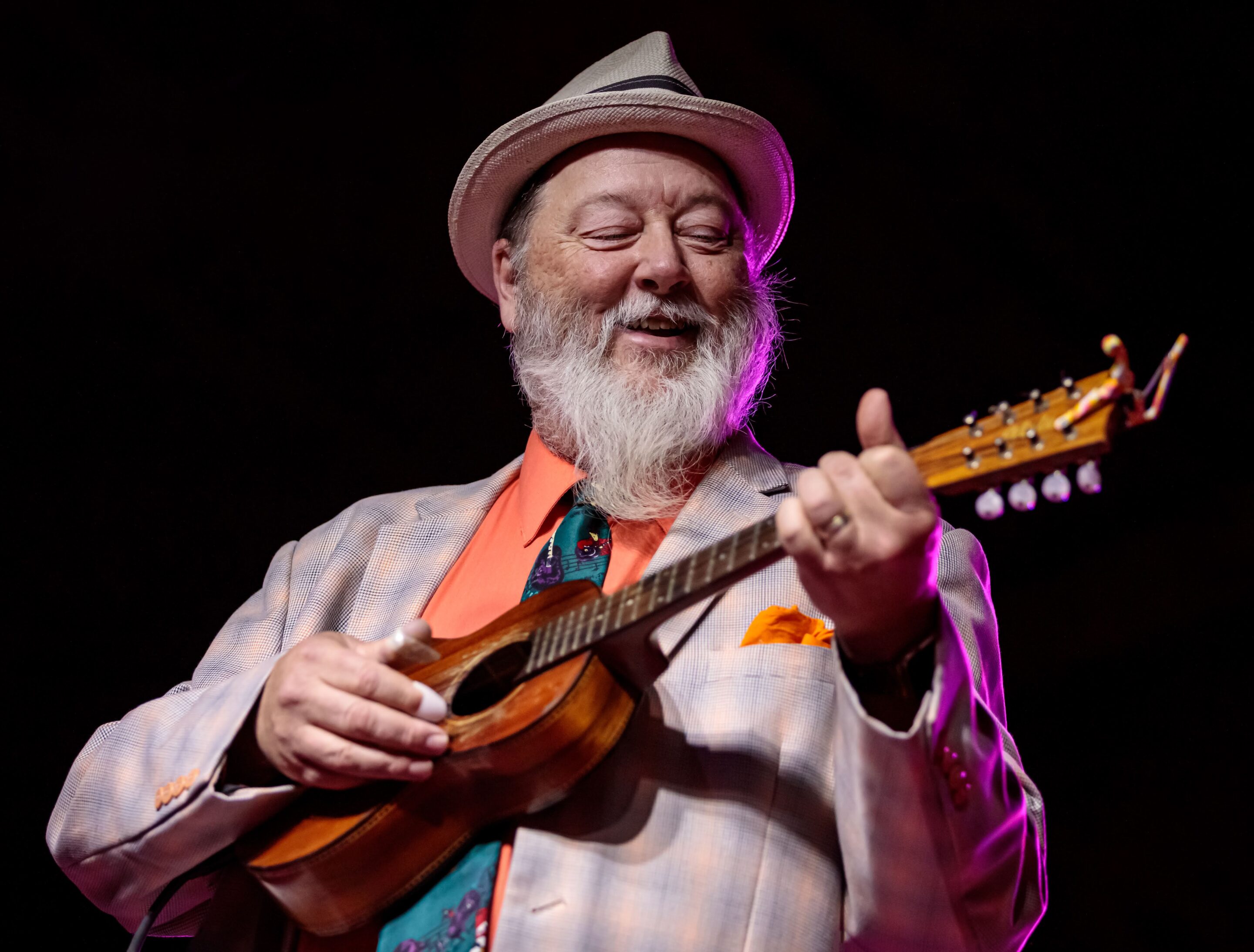 Photo of Kevin Russell, the charismatic frontman with colorful suits and extravagant shoes, of Shinyribs playing a ukulele.